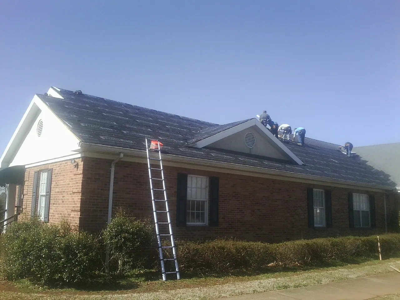 Crew tearing shingles off a brick ranch roof with a ladder set — Metal Roof Repair work by our crew in Westfield